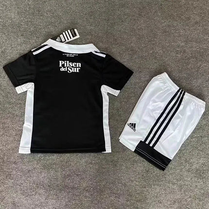 Kit maglia bimbo colo-colo 2022/23 vista retro con maglia nera e scritta pilsen del sur e pantaloncini adidas neri