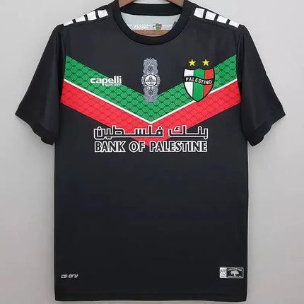 Maglia nera deportivo palestino trasferta 2022 23 con righe diagonali verdi e rosse, stemma e sponsor sul davanti