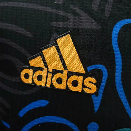 Maglia real madrid allenamento 2022 23 con logo adidas ricamato in oro su tessuto nero con pattern blu graffiti