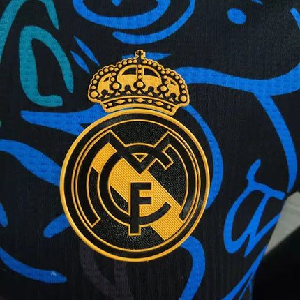 Maglia real madrid allenamento 2022 23 con stemma ricamato dorato su sfondo nero con motivi astratti blu